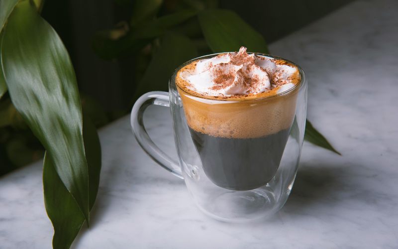 A small espresso cup with a shot of dark espresso, topped with a generous swirl of white whipped cream.